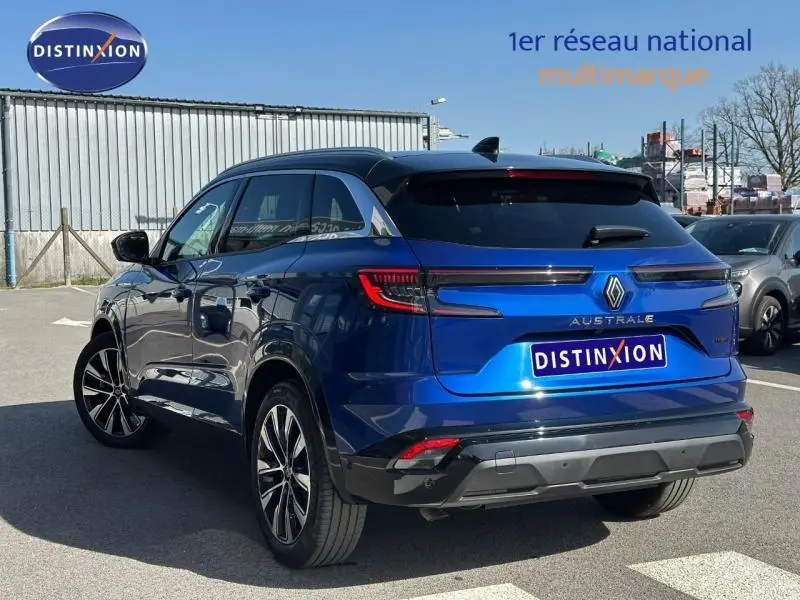 Vue 3/4 arrière d'un Renault Austral Bleu Iron 2025 avec feux arrière LED et logo distinctif sur un parking extérieur.