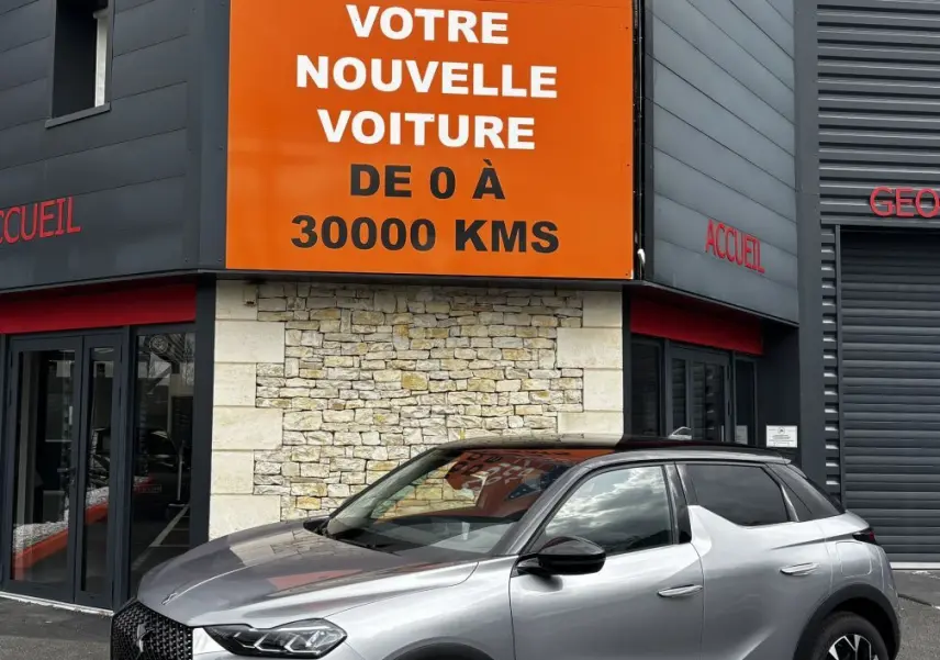 DS3 gris clair vue 3/4 avant droit, avec toit noir et jantes alliage distinctives, devant un panneau orange Distinxion.