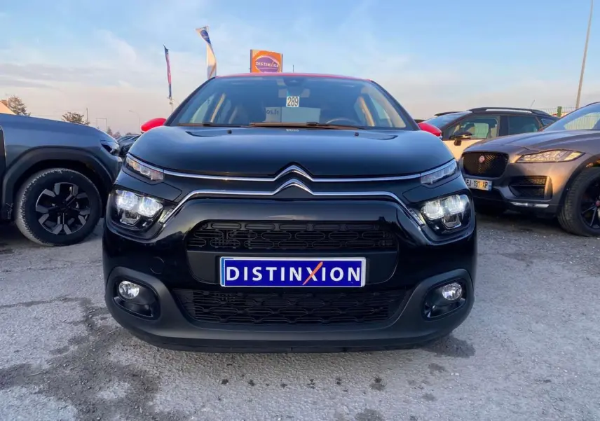 Vue avant d'une Citroën C3 Shine 2023 noire avec toit rouge, phares LED allumés sur parking extérieur.