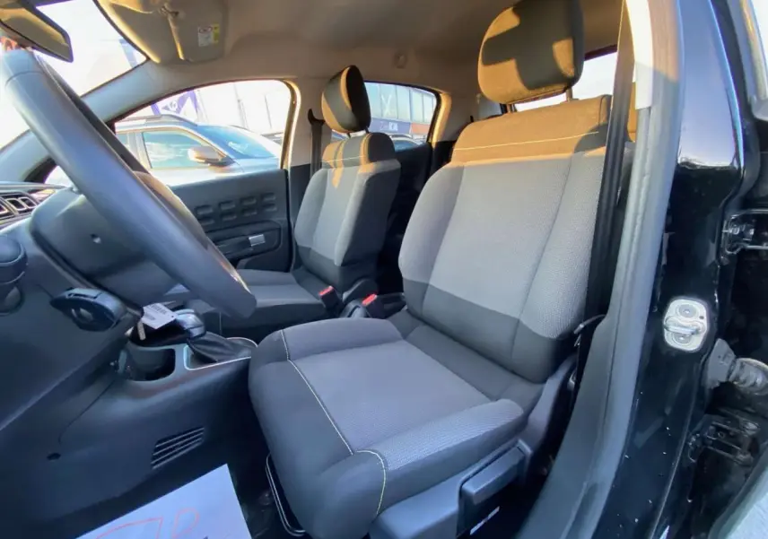 Vue intérieure côté conducteur de la Citroën C3 2023 noire, montrant les sièges avant gris et la console centrale.