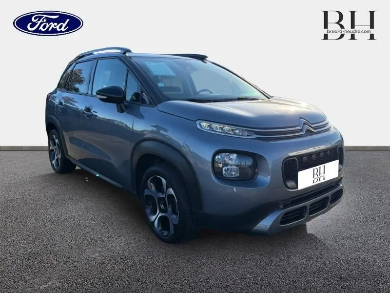 Citroën C3 Aircross gris acier vue 3/4 avant droit, avec barres de toit et jantes diamantées noires.