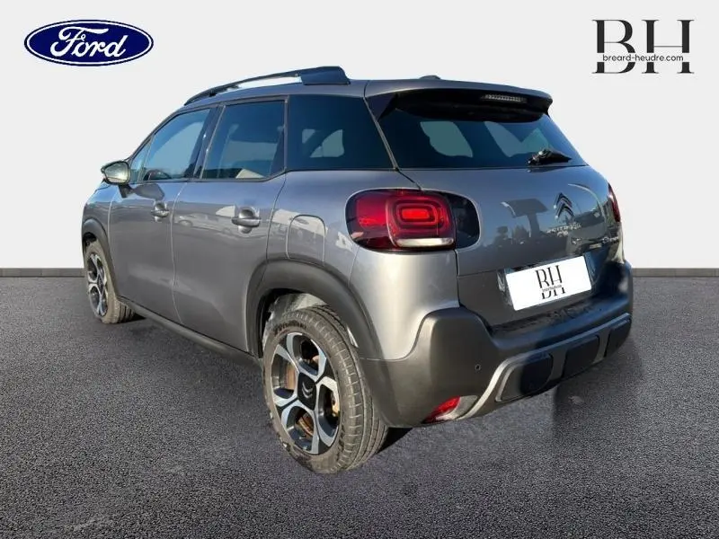 Vue 3/4 arrière droite d'un Citroën C3 Aircross gris acier avec barres de toit et jantes diamantées noires.