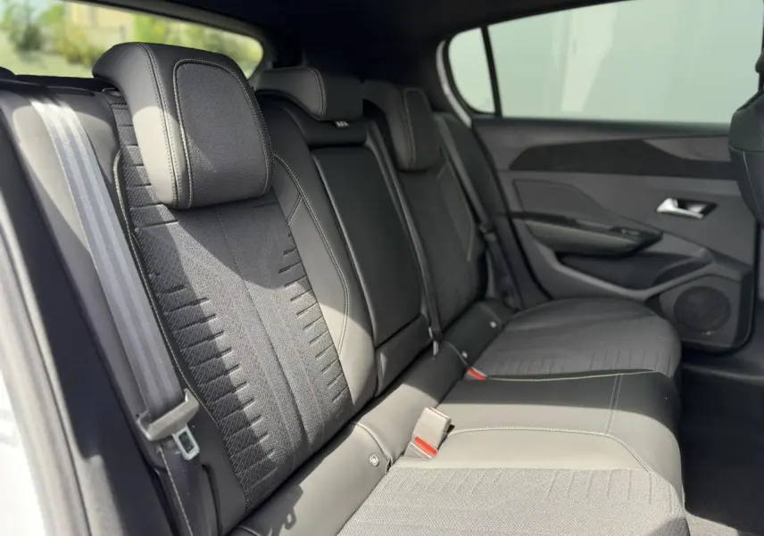 Vue latérale intérieure montrant la banquette arrière tissu noir avec surpiqûres vert Adamite de la Peugeot 308 Hybrid 2026.