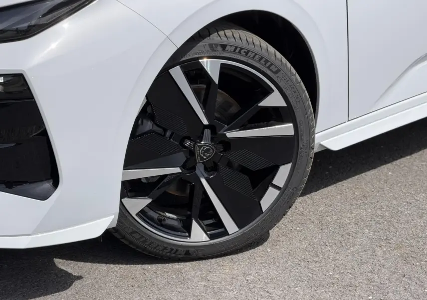 Gros plan sur la roue avant droite de la Peugeot 308 NV Hybrid blanche avec jante alliage bi-ton noir brillant et argent.