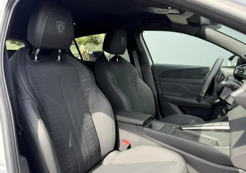 Vue intérieure côté conducteur de la Peugeot 308 NV Hybrid 145 GT avec sellerie noire et surpiqûres vert Adamite.
