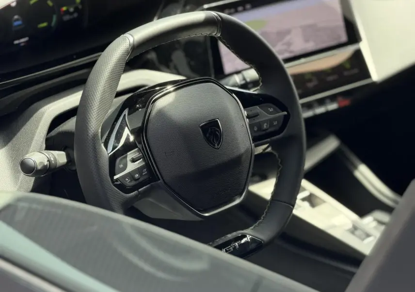 Gros plan sur le volant cuir noir GT avec logo Peugeot, tableau de bord numérique et écran tactile du Peugeot 308 Hybrid.