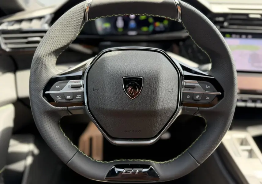 Gros plan sur le volant cuir noir du Peugeot 308 GT avec surpiqûres vertes et logo central lion brillant.