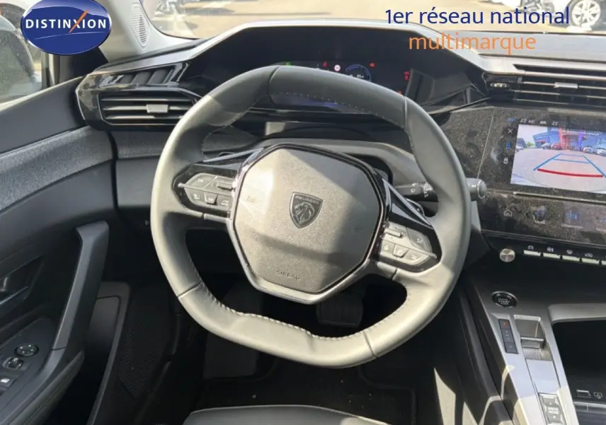Vue intérieure centrée sur le volant cuir du Peugeot 308 Allure Hybrid 2025 avec écran tactile et caméra de recul affichée.