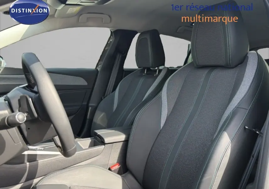 Vue intérieure côté conducteur de la Peugeot 308 Allure Hybrid 145 e-DCS6, sièges tissu et cuir gris avec surpiqûres bleues.