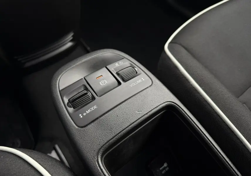 Gros plan sur la console centrale de la Fiat 500 électrique blanche, avec commandes e-mode et volume, sièges noirs à liseré blanc.