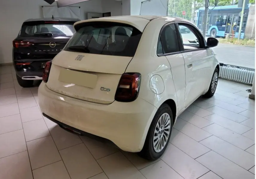 Vue 3/4 arrière droite d'une FIAT 500 électrique blanche 2024 dans un showroom avec feux arrière foncés.