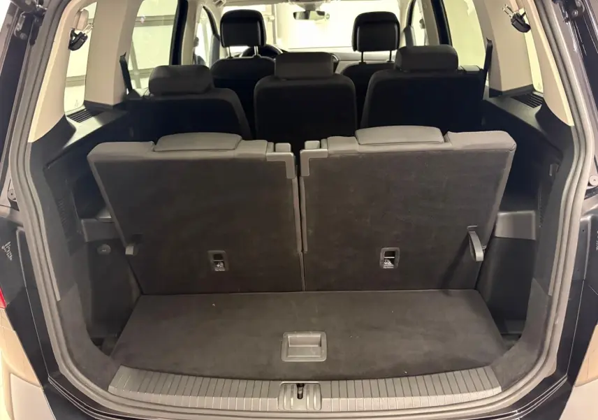 Coffre ouvert vue arrière d'un Volkswagen Touran noir intense nacré, montrant les sièges arrière rabattus partiellement.