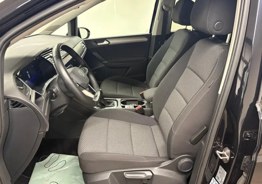 Intérieur avant droit du Volkswagen Touran noir intense nacré, sièges tissu gris et tableau de bord moderne.