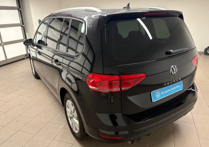 Vue 3/4 arrière gauche d'un Volkswagen Touran noir intense nacré avec hayon électrique et vitres teintées dans un garage.