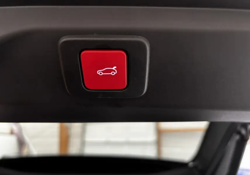 Bouton rouge d'ouverture électrique du coffre visible en gros plan à l'intérieur du hayon du Peugeot 3008 vert.