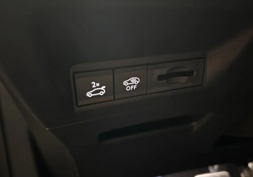 Gros plan sur les boutons de commande intérieurs du Peugeot 3008 hybride 2025, avec éclairage blanc sur fond noir.