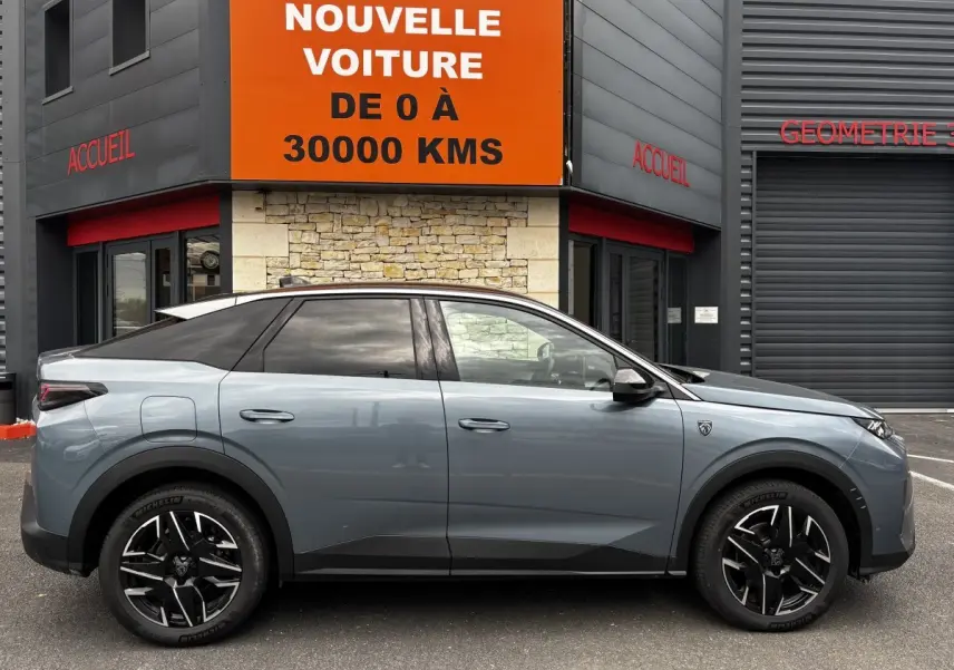 Profil droit d'un Peugeot 3008 gris métallisé, avec jantes noires et toit noir, stationné devant un bâtiment commercial.