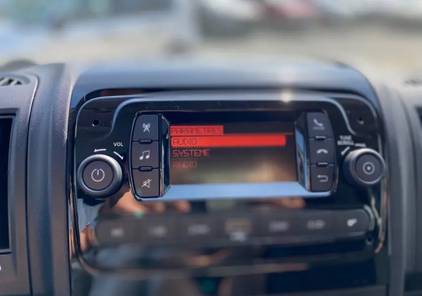 Gros plan sur la console centrale du Citroën Jumper 2023, écran audio avec menu en rouge et boutons noirs.