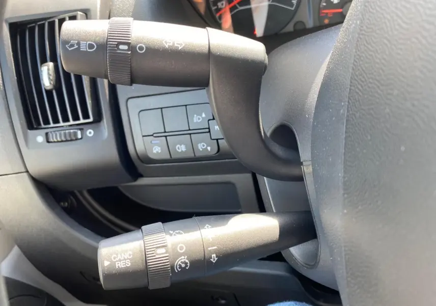 Gros plan sur les commandes au volant du Citroën Jumper 2023, avec tableau de bord et manettes noires visibles.