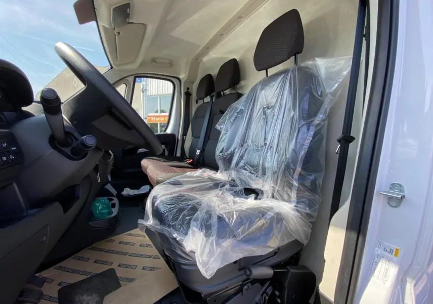 Vue intérieure côté conducteur du Citroën Jumper blanc 2023, sièges avant avec protection plastique et volant visible.