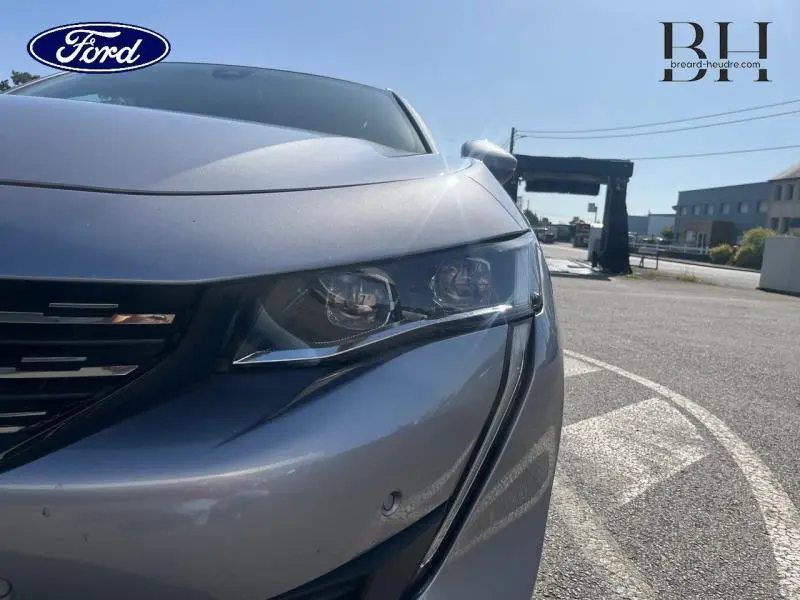 Gros plan sur l'avant droit d'une Peugeot 508 SW gris Artense, mettant en valeur le phare et la calandre chromée.