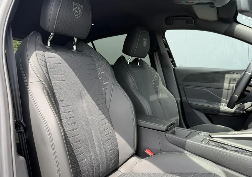 Vue intérieure côté gauche des sièges avant noirs avec surpiqûres vertes et logo Peugeot embossé sur appuie-têtes.