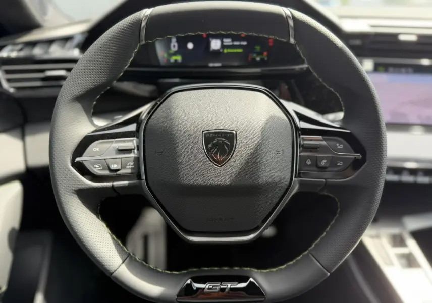 Vue rapprochée du volant compact GT en cuir noir avec surpiqûres vert Adamite et logo Peugeot au centre.