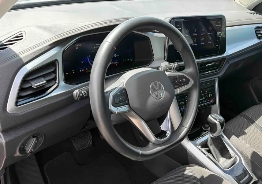 Vue intérieure centrée sur le volant cuir multifonctions et la console centrale du Volkswagen T-Roc 2025 noir avec boîte manuelle.