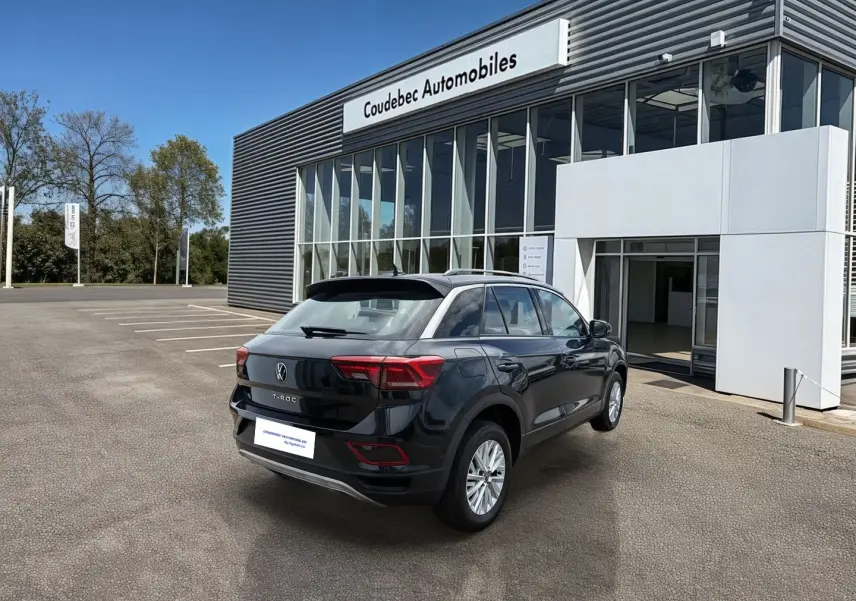 Vue 3/4 arrière droite d'un Volkswagen T-Roc noir stationné devant un bâtiment commercial moderne.