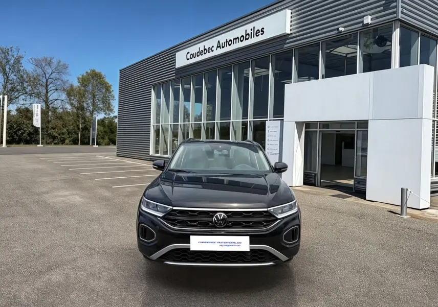Vue de face du Volkswagen T-Roc noir 2025 garé devant un bâtiment moderne de concession automobile.