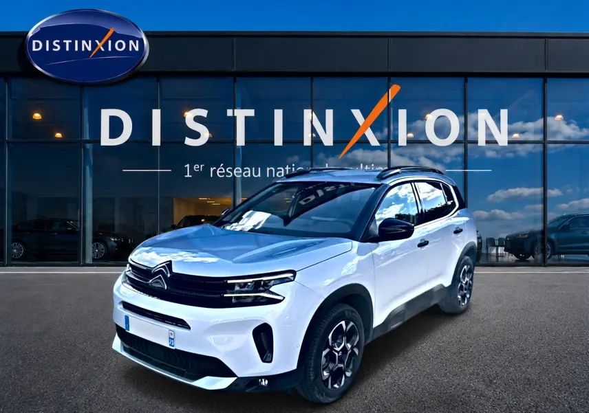 Citroën C5 Aircross blanc en 3/4 avant droit, avec jantes alu et barres de toit visibles devant showroom Distinxion.