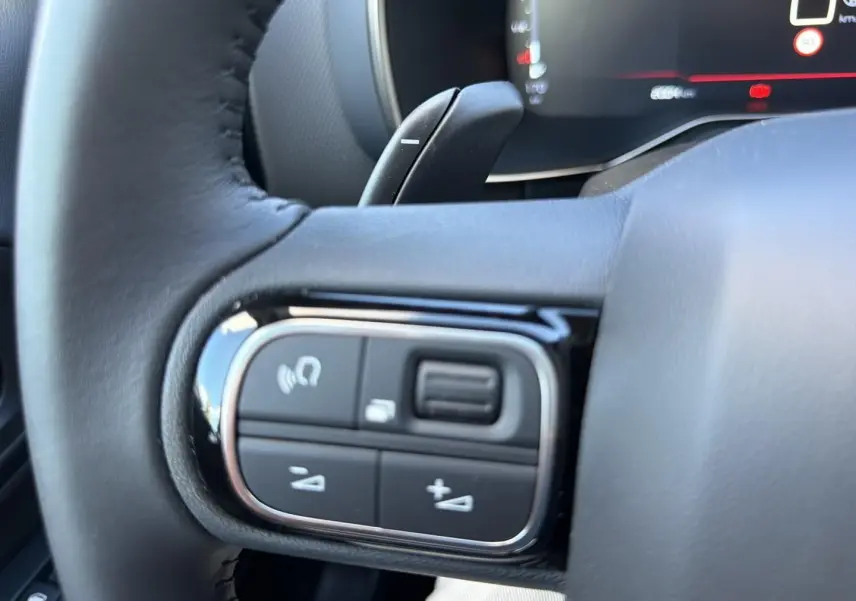 Gros plan sur les commandes multifonctions noires du volant cuir du Citroën C5 Aircross 2025, version diesel blanche.