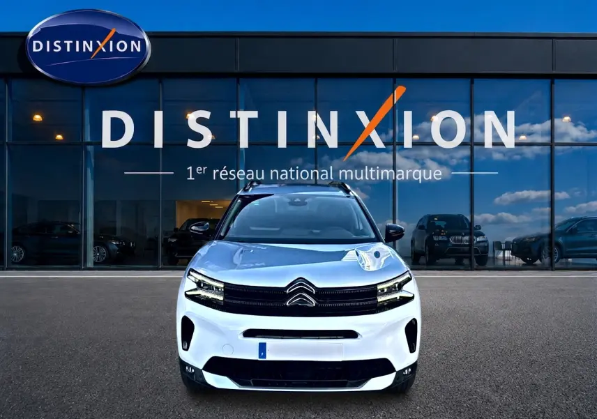 Vue frontale d'un Citroën C5 Aircross blanc 2025 garé devant une vitrine avec logo Distinxion.