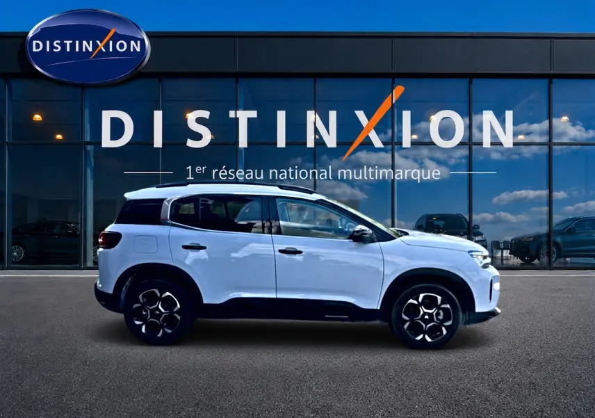 Profil droit d'un Citroën C5 Aircross blanc 2025 avec jantes alu et barres de toit devant une vitrine Distinxion.