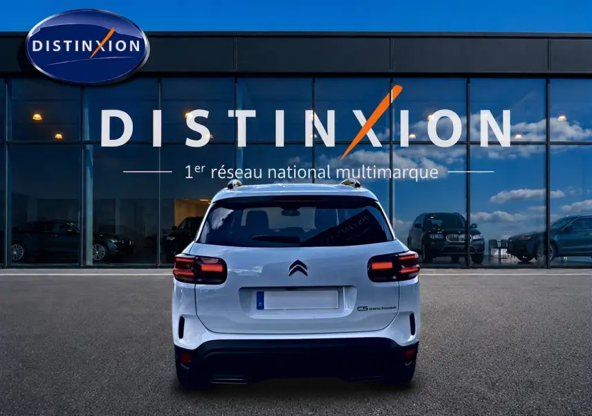 Vue arrière d'un Citroën C5 Aircross blanc 2025 stationné devant une vitrine avec logo Distinxion.