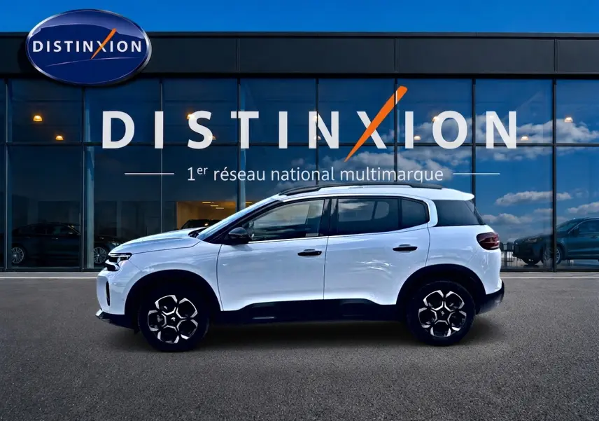 Vue de profil côté gauche d'un Citroën C5 Aircross blanc 2025 devant une vitrine avec logo Distinxion.