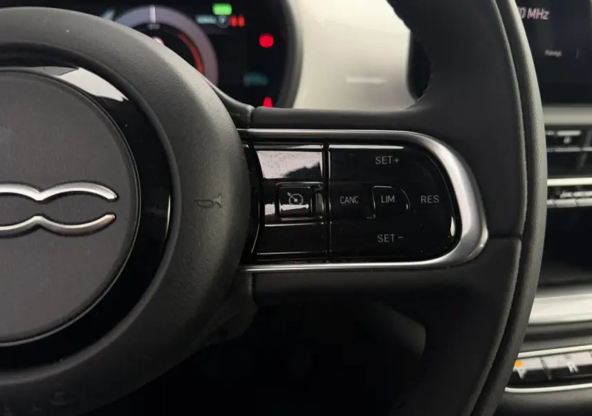 Gros plan sur le volant noir de la Fiat 500 électrique 2024, avec commandes de régulateur de vitesse sur la droite.