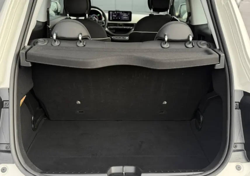 Coffre ouvert vu de l'arrière d'une Fiat 500 électrique blanche, montrant l'espace de chargement et les sièges avant.