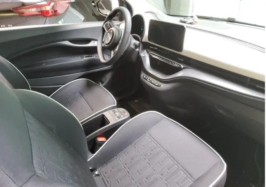 Intérieur de la Fiat 500 électrique 2024 vu côté conducteur, avec tableau de bord clair et sièges noirs à surpiqûres blanches.