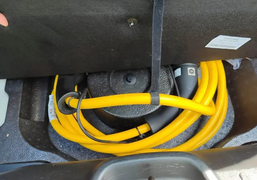Câble de recharge jaune enroulé dans le coffre de la Fiat 500 électrique blanche, vue rapprochée intérieure.