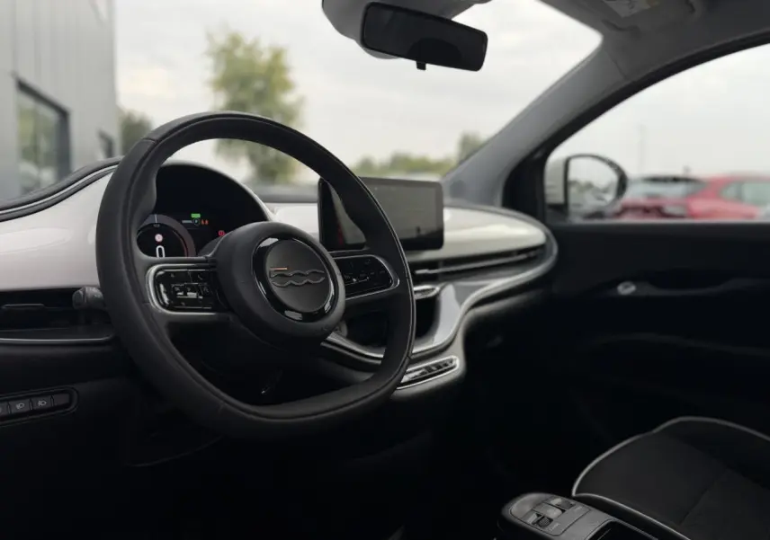 Vue intérieure côté conducteur de la Fiat 500 électrique 2024, volant noir avec tableau de bord digital et écran central.