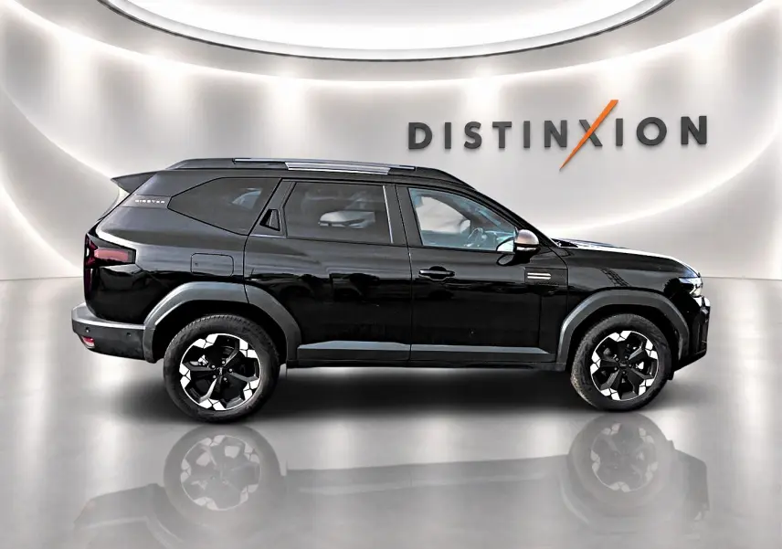 Profil droit du Dacia Bigster noir 2025 avec jantes alu noires et barres de toit, dans un showroom épuré.