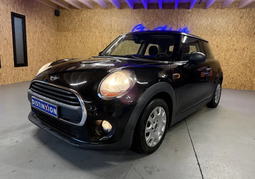 Mini One noire vue 3/4 avant droit en intérieur, phares et antibrouillards allumés, calandre chromée visible.