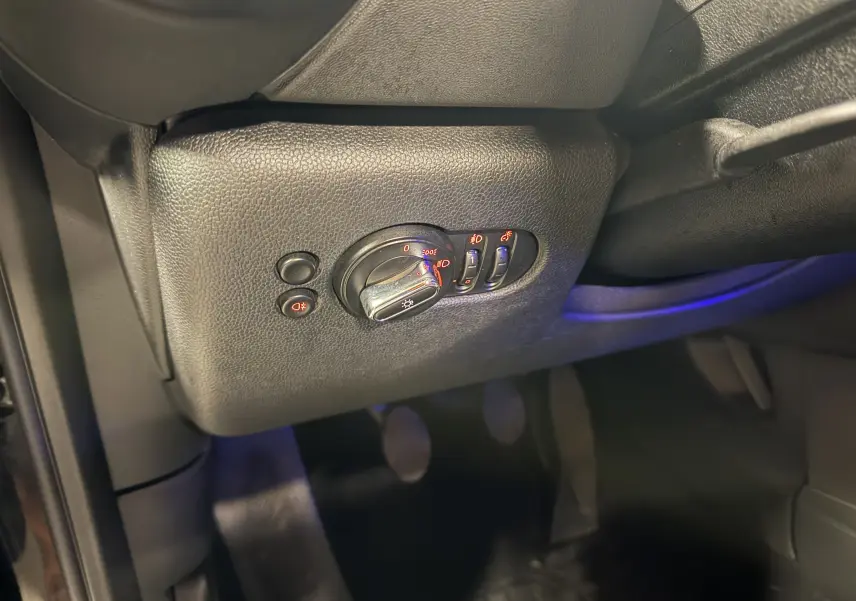 Détail du panneau de commande des phares avec interrupteurs éclairés sur le côté gauche intérieur d'une MINI noire.