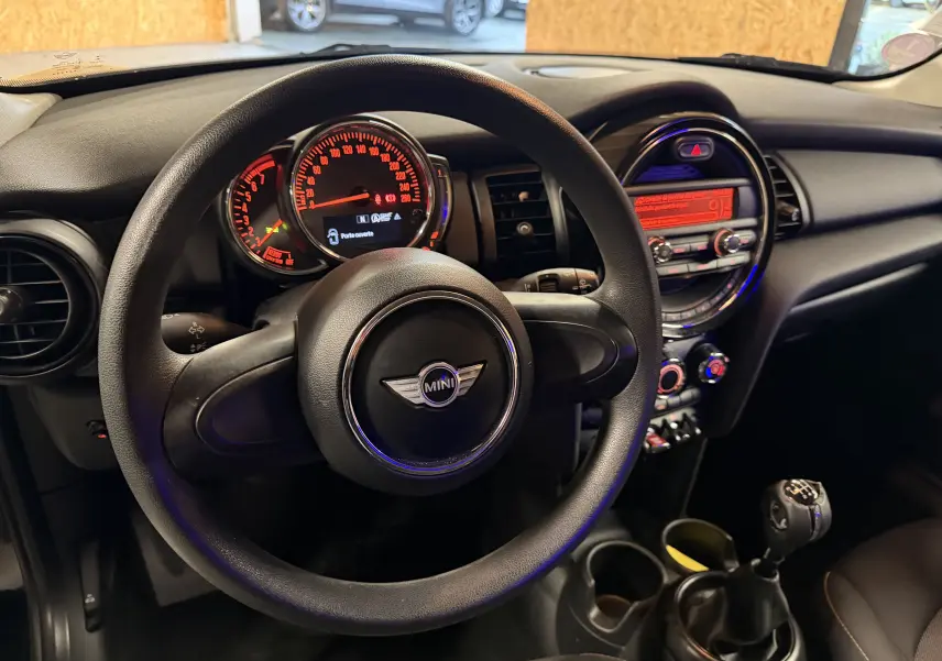 Vue intérieure centrée sur le volant et le tableau de bord d'une MINI noire avec boîte manuelle et écran central éclairé.