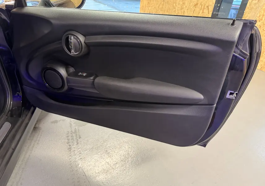 Vue intérieure de la porte côté gauche noire d'une MINI 1.5i 75CV ONE, avec commande de vitre électrique et haut-parleur intégré.