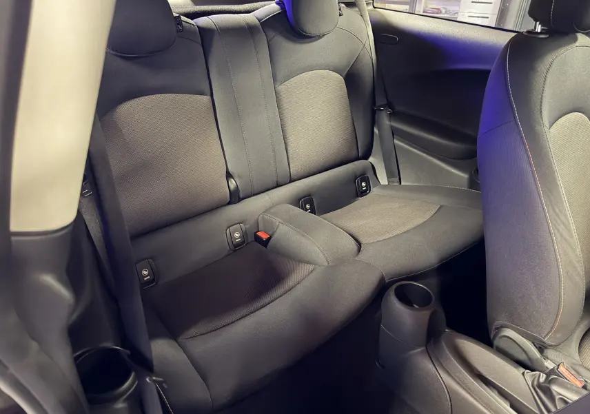 Vue intérieure de l'arrière d'une MINI 1.5i noire, montrant les sièges arrière en tissu gris avec appuie-têtes et ceinture de sécurité.