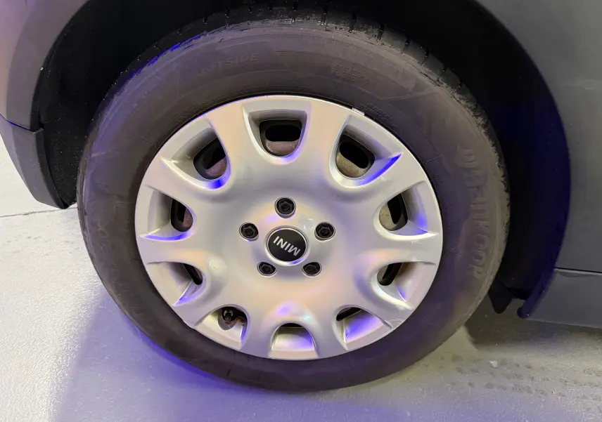 Gros plan sur la roue avant gauche d'une MINI noire, mettant en valeur le pneu et l'aile du véhicule.