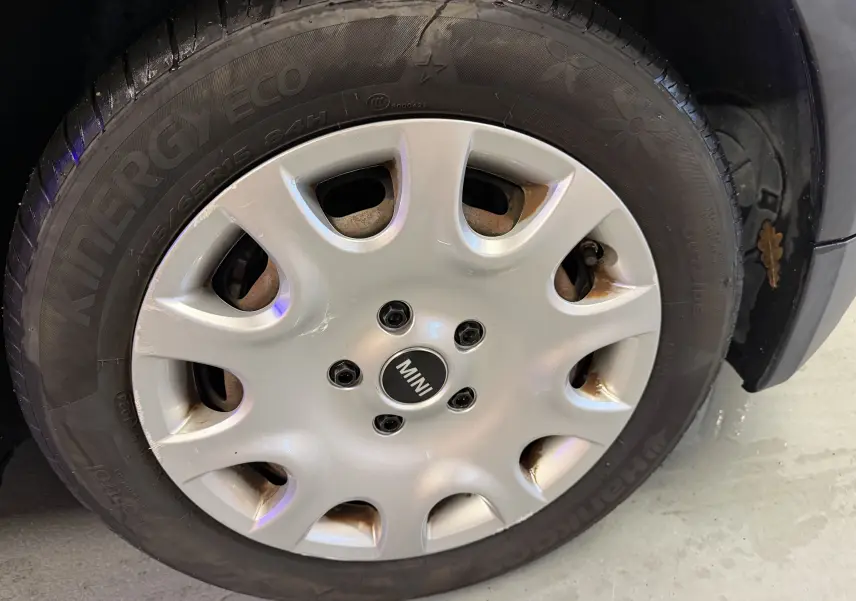 Gros plan sur la roue avant droite d'une MINI noire, mettant en valeur la jante argentée avec logo MINI au centre.