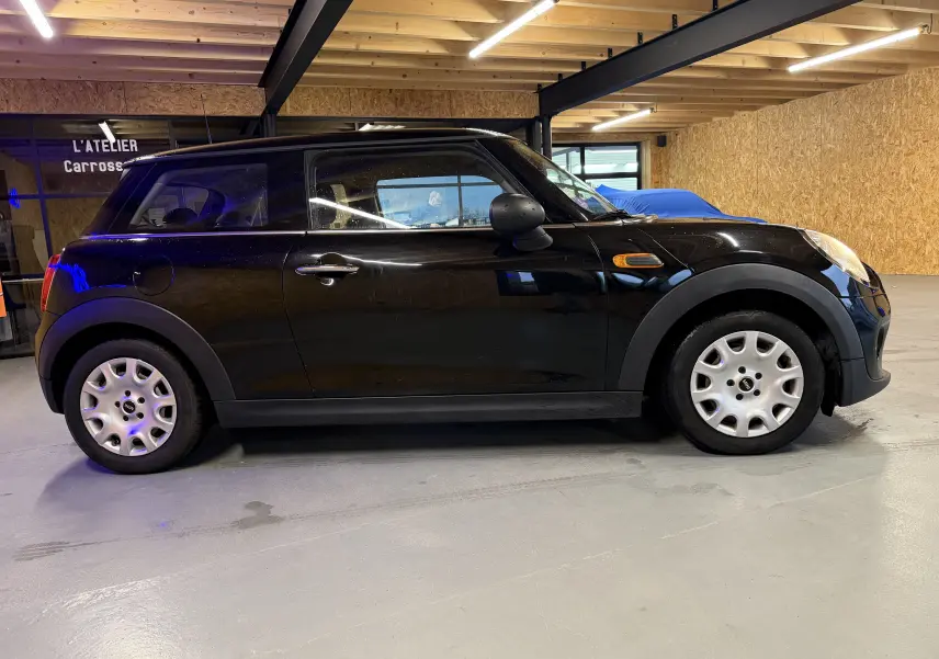 Vue de profil côté droit d'une MINI noire 3 portes, stationnée en intérieur avec jantes acier et clignotant latéral orange.